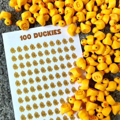 100 tiny yellow numbered ducks spread out next to a tracking sheet, part of the Mega Hunt Pack