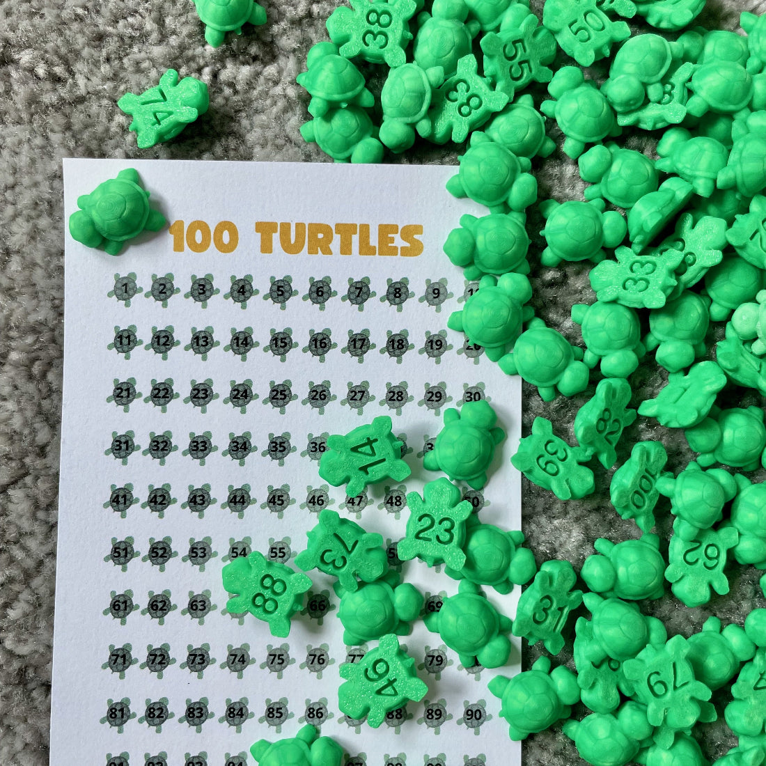 Green numbered turtles scattered over a 100 Turtles tracking sheet with turtle illustrations