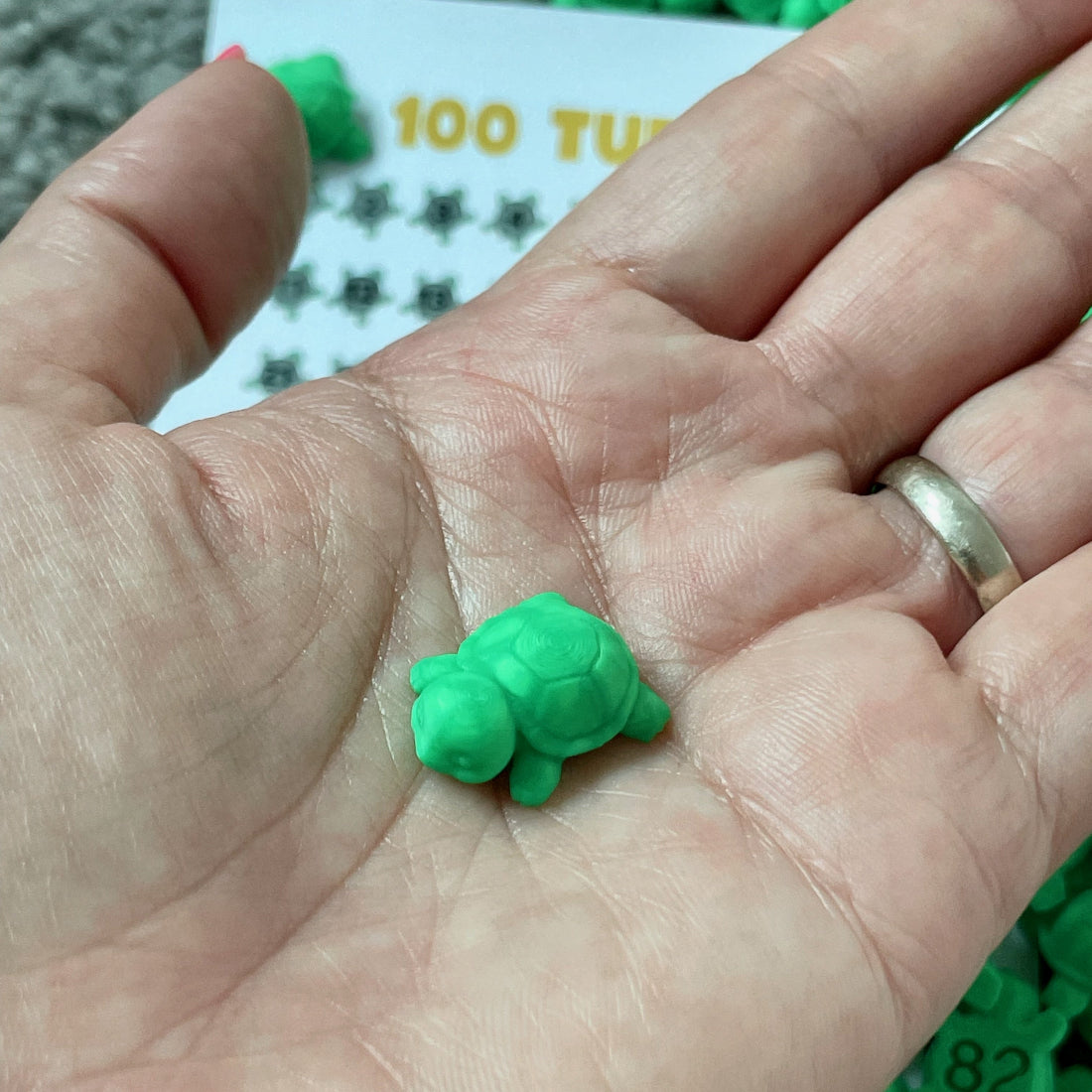 Single tiny green turtle in the palm of a hand, showing its small size and 3D printed detail