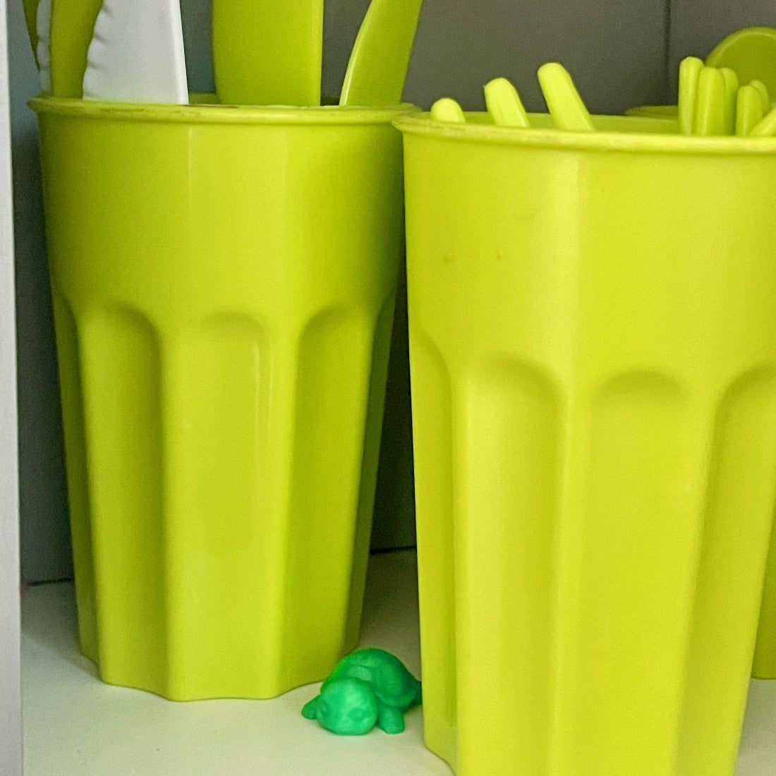 Tiny green turtle hidden between green cups on a kitchen shelf