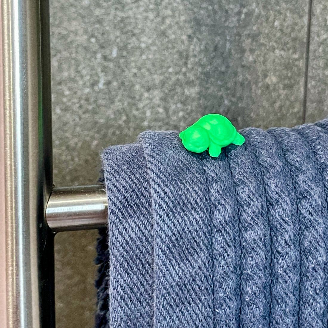 Tiny green turtle hidden on top of a folded towel on a bathroom towel rack