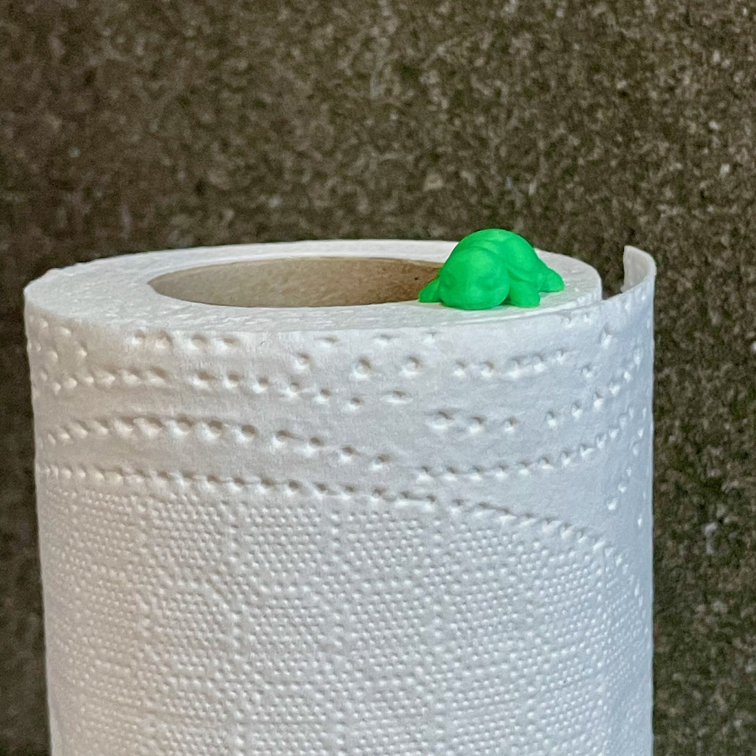 Tiny green turtle peeking out from the top of a toilet paper roll