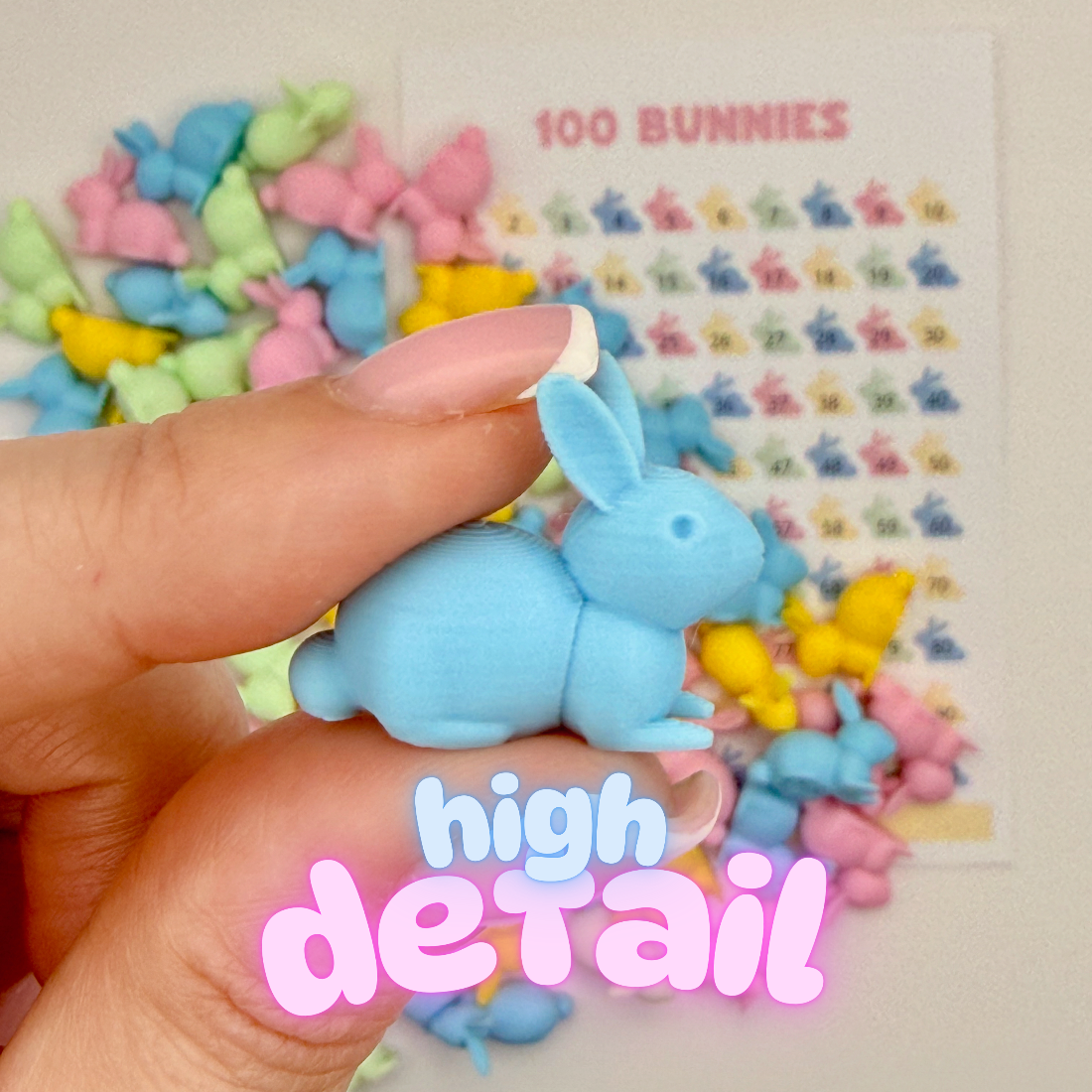 Hand holding a small blue bunny figure showing the 3D printed detail, with more pastel bunnies in the background