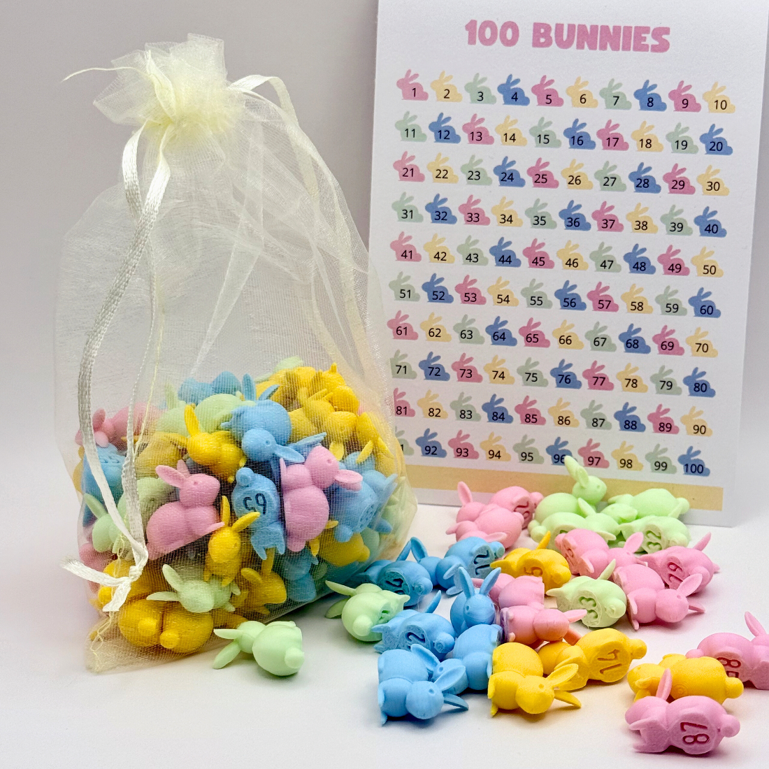 Pastel numbered bunnies inside a sheer mesh bag with satin ribbon, next to a 100 Bunnies tracking sheet